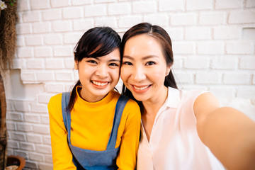 face of smiling happy asian teenage daughter and asian middle-aged mother looking at mobile phone in
