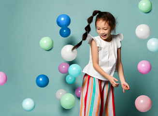 Playful asian Korean kid girl with long black plait is having fun surrounded by colorful air balloons