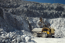 Mining Excavator And Heavy Mining Truck In A Quarry For The Extraction Of Limestone On The Background Of Rocky Terrain In Sunny Weather, Close-up.