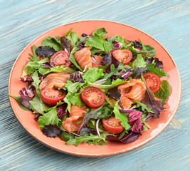 Salmon salad, cherry tomatoes, spinach, radicio, lollo. Home made vegetarian salmon salad. Seafood tasty concept. Mix leaves greens with salmon fish in plate on blue wood, closeup