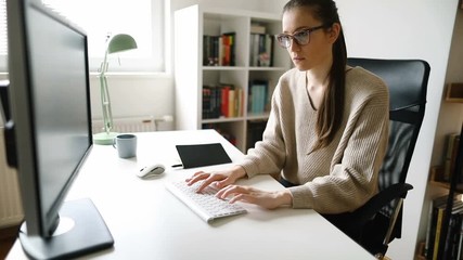 Wall Mural - Focused young woman working on desktop PC. Young businesswoman working on computer at her home office