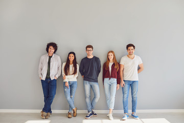 group of young people in casual clothes smiling while standing against gray background.