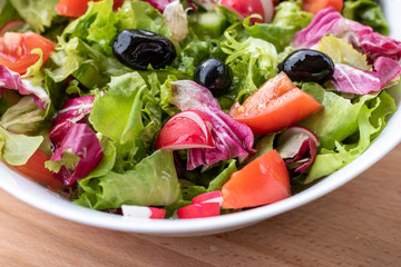 Green vegan salad from green leaves mix and vegetables in white bowl.Summer Easter diet salad dish of lettuce, radicchio, Lollo Rossa, endives, radishes, green onions, cucumbers, olives and tomatoes