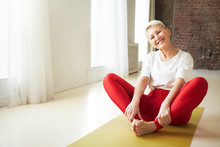 Sporty 50 Year Old Gray Haired Woman Sitting Barefooted On Yoga Mat Indoors Doing Bound Ngle Pose Which Helping To Relieve Symptoms Of Menopause. Aging, Maturity, Wellness And Health Concept