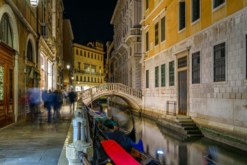 Fototapete - Narrow canal with gondola and bridge in Venice, Italy. Architecture and landmark of Venice. Cozy night cityscape of Venice.