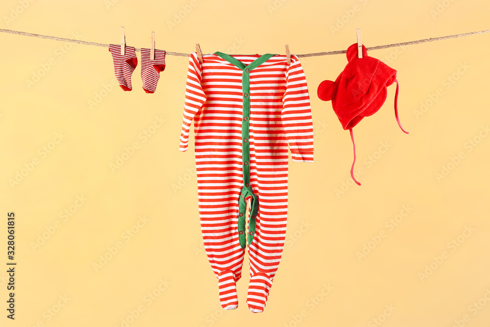 Baby clothes and accessories hanging on rope against color background