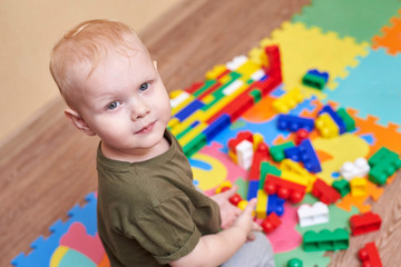 Wall Mural - A two-year-old boy plays with a colorful constructor set on the floor of a house.