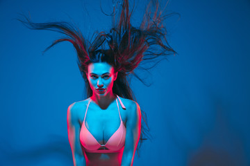 Attractive brunette model on blue studio background in neon light. Beautiful women in underwear posing with flying hair and dark make up. Concept of sensuality, style, fashion industry, characters.