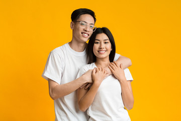 Young asian man and woman hugging on yellow