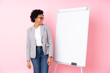 Wall Mural - African american business woman giving a presentation on white board over isolated pink background looking side