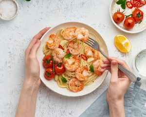 Canvas Print - Pasta bavette with fried shrimps, bechamel sauce. Woman hands in frame, girl eats pasta, top view