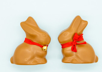 Wall Mural - Two chocolate eastern bunnies with red bows on a blue background. Isolated. Copy space. 