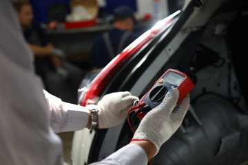 Close-up view of auto mechanic using red voltmeter to check the voltage level in a car battery. Automobile repair service station and special equipment for vehicle