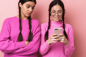 Poster - Image of upset girl standing by her happy female friend with cellphone