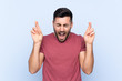 © luismolinero - Young handsome man with beard over isolated blue background with fingers crossing
