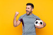 © luismolinero - Man over isolated yellow background with soccer ball celebrating a victory