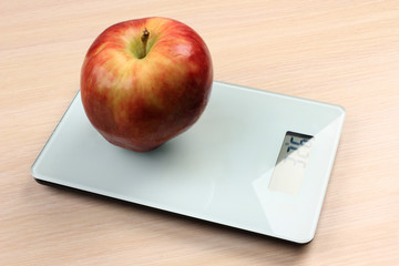 Big red apple on a kitchen scale on a wooden table