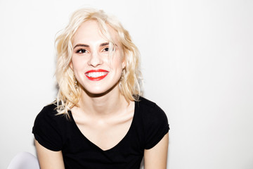 young smiling blonde girl in a black t-shirt on a white background, studio fashion photo with copy space