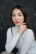 Portrait of a young Asian girl holding her hands to her face, looking directly at the camera. She's wearing a light turtleneck. The concept of skin care and hair              