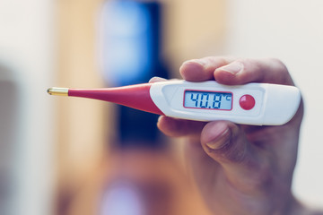 Flu and corona concept: Man is holding a fever thermometer in his hand, close up