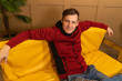 © Anton Dios - A confident, happy young man is resting on the couch at home. A visiting man in casual clothes while sitting on a yellow sofa at home