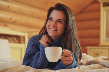 Sticker - Young woman in warm sweater with cup of hot drink on bed at home