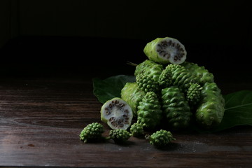 Noni fruit, herbs and sliced on wood, on a black background. Dark tones, rich in nutrients. Antioxidants.