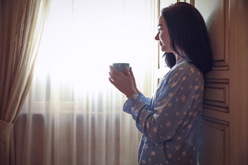 Sticker - Young woman with drink near window at home. Lazy morning