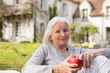 © PhotoAlto - Portrait of smiling senior woman holding an apple while sitting in garden