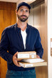 © PhotoAlto - Portrait of delivery man standing in corridor with parcels