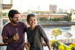 © PhotoAlto - Smiling young couple holding with beer bottles while standing on balcony