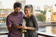 © PhotoAlto - Happy young couple using smartphone while standing on balcony