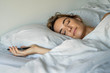 © PhotoAlto - Content young woman holding smartphone while sleeping on bed in bedroom