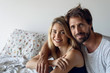 © PhotoAlto - Portrait of smiling young couple sitting on bed in bedroom