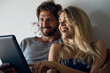 © PhotoAlto - Happy young couple watching movie on digital tablet in bedroom