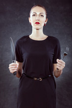 Portrait Of A Beautiful Young Woman On A Black Background With A Knife And A Fork In Her Hands.