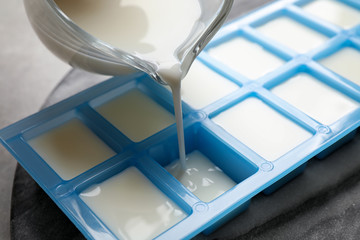 Pouring milk into ice cube tray at table, closeup