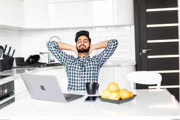 Wall Mural - Happy relaxed indian man using laptop in the kitchen