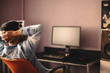 © Cavan Images - Man relaxing sitting on chair by computer with hands behind head