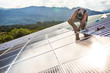 © Cavan Images - Worker uses hand tool to secure solar panels on roof of building.