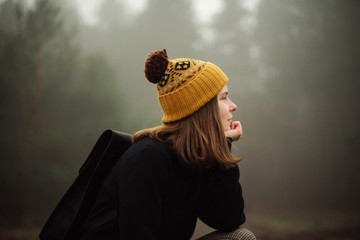 Thoughtful woman sitting by forest in foggy weather