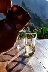 Wall Mural - Man pouring white wine from clay jug into glass on terrace with view on green landscapes of small mountain village Masca on Tenerife, Spain