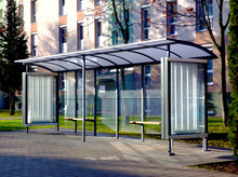Clear Glass And Aluminum Frame Structure Bus Shelter At Bus Stop In Residential Area. Bare Trees And Green Grass In The Background. Public Transportation. Ad And Copy Space.