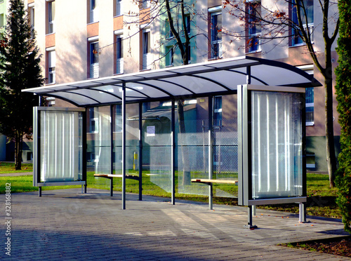 clear glass and aluminum frame structure bus shelter at bus stop in residential area. bare trees and green grass in the background. public transportation. ad and copy space.