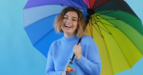 Wall Mural - Rainbow umbrella. Portrait of happy smiling young sexy girl rainbow umbrella in blue sweater on blue background. Pleasure. Emotions of people. Monotone. Copy space. Blue pantone