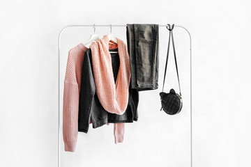 Wall Mural - Female clothes in pastel pink and gray color on hanger on white background. Jumper, shirt, jeans and scarf. Spring/autumn outfit. Minimal concept.