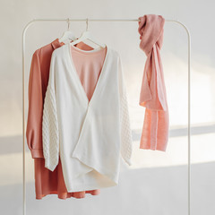 Wall Mural - Female clothes in pastel pink color on hanger on white background. Elegant dress, jumper, shirt and scarf. Spring cleaning home wardrobe. Minimal concept.