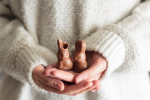 Woman Hands Holding Two Chocolate Easter Rabbits, One With A Bite
