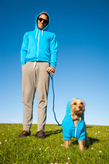 Small dog standing outdoors with his best friend owner in matching blue hoodies on bright green field