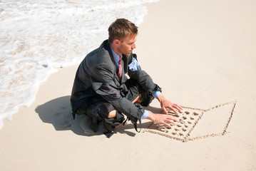 Businessman working on his sand laptop next to foamy white waves washing up the beach